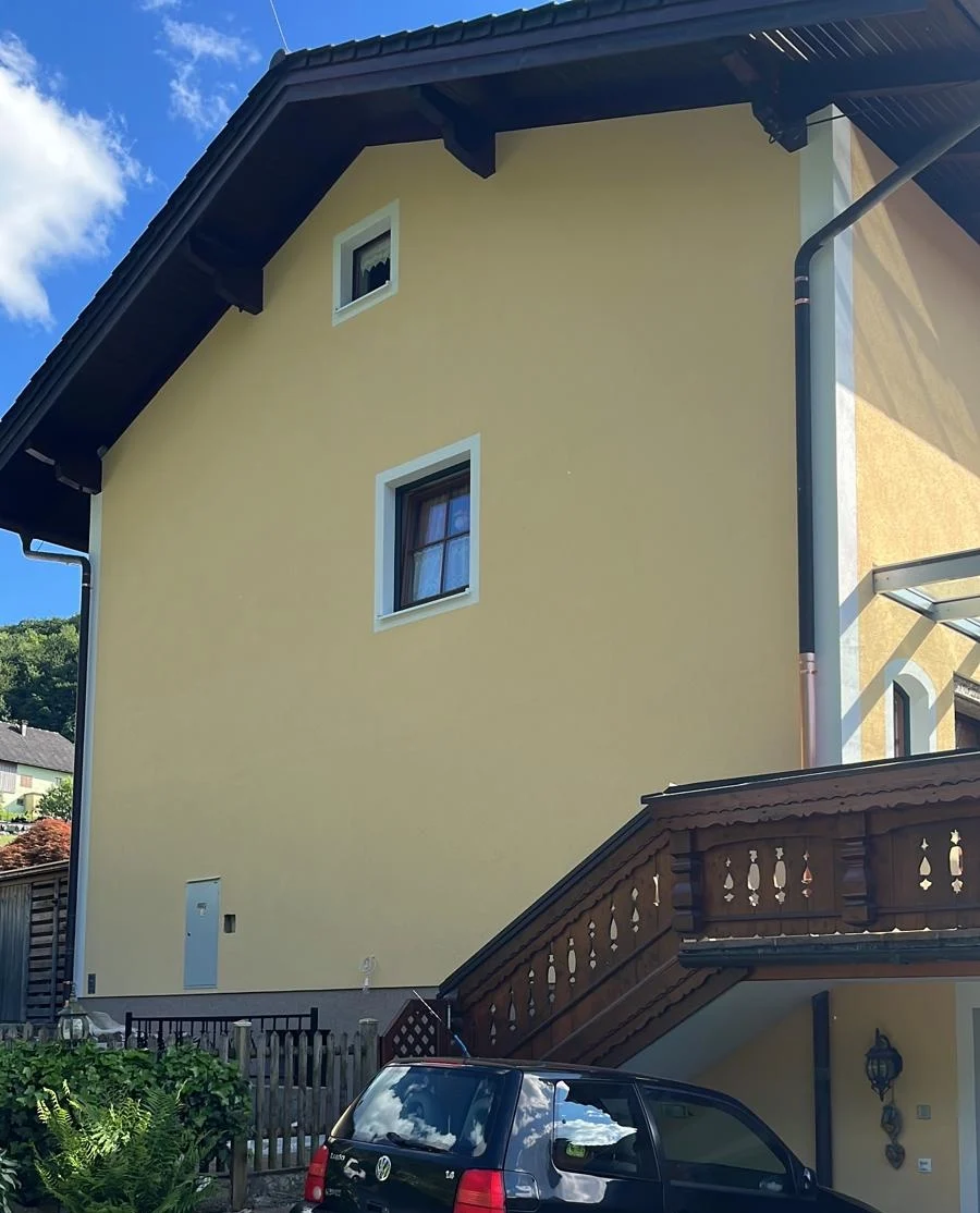 Ausgeführte Putzfassade mit hellgelber Oberfläche und weißen Fensterfaschen